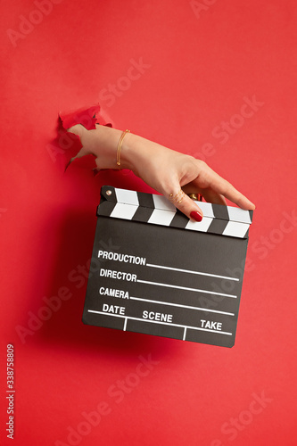 Fényképezés Woman hand holding movie clapper through the hole in red paper background