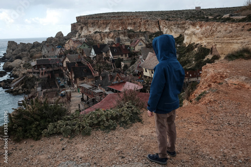 A child with a hoodie is watching of the Popeye Village (Sweethaven Village) in Malta from above.
