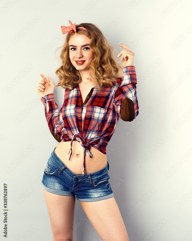 Pin-up girl with curly blond hair with red checkered bow and shirt wearing jeans shorts. Pin-up girl with curly blond hair with red checkered bow and shirt wearing jeans shorts.