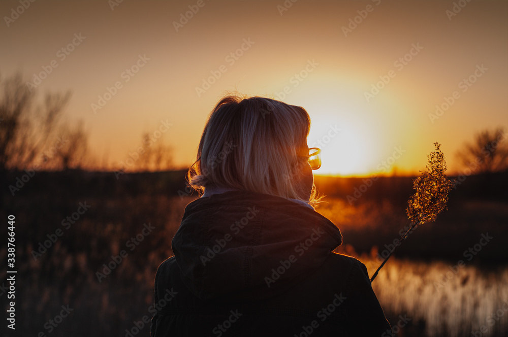 Beautiful girl at sunset in the autumn. Young woman in coat near the pond from behind.