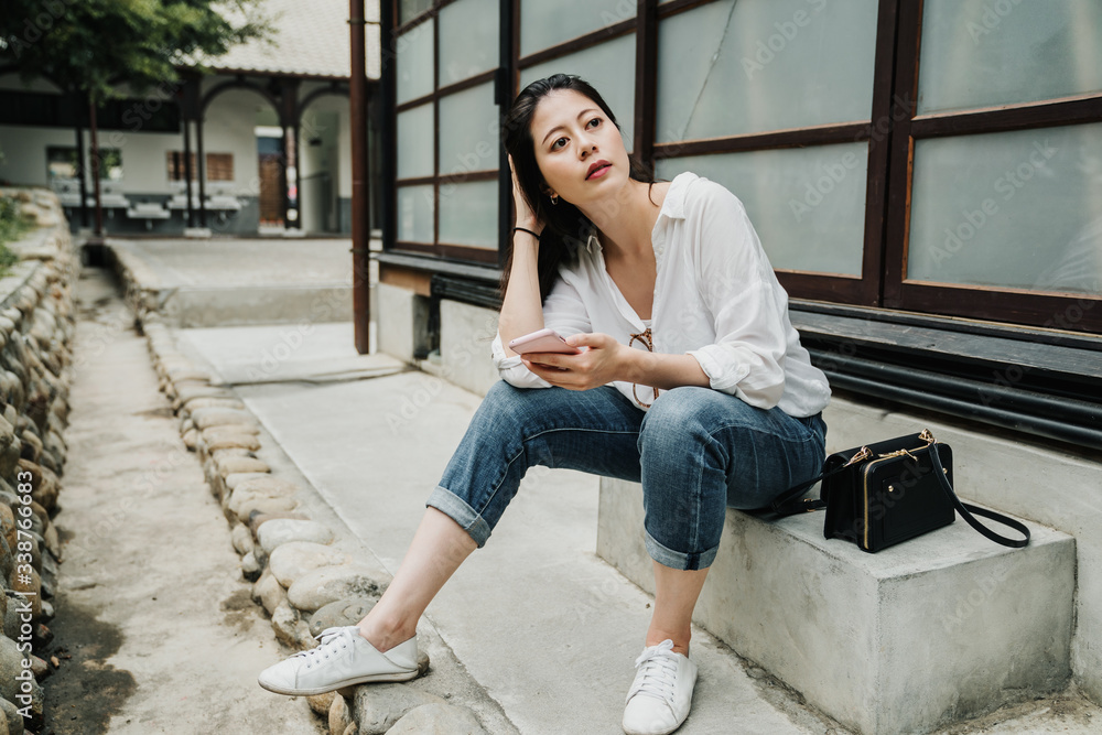 tourist Asian chinese girl using mobile phone enjoying summer travel holidays. young woman visiting old town in kyoto japan. beautiful female sitting on stone bench chair with cellphone and bag.