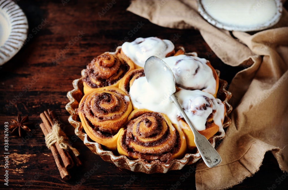 Cinnamon Rolls Baked in Ceramic Mold with Cream Cheese Icing on a Dark Wooden Background