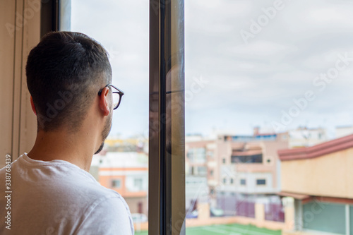 Bored man in quarantine, homebound, looking out the window at the street, from where he sees an empty football ground. photo