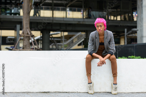 Young rebellious Asian businesswoman with pink hair sitting outdoors