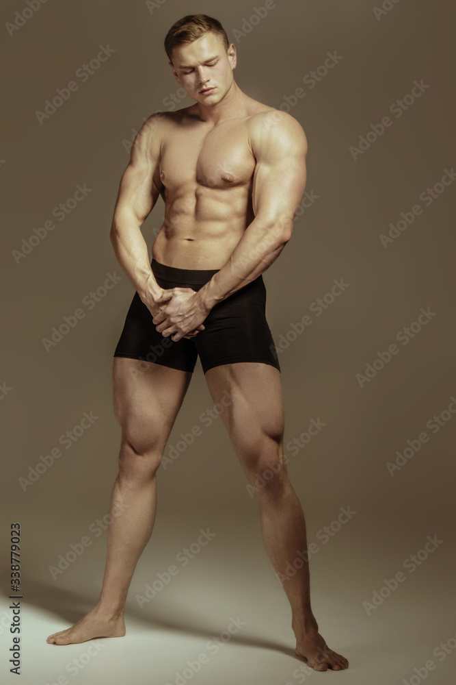 Strong stripped muscle male model in black underwear on gray isolated font background