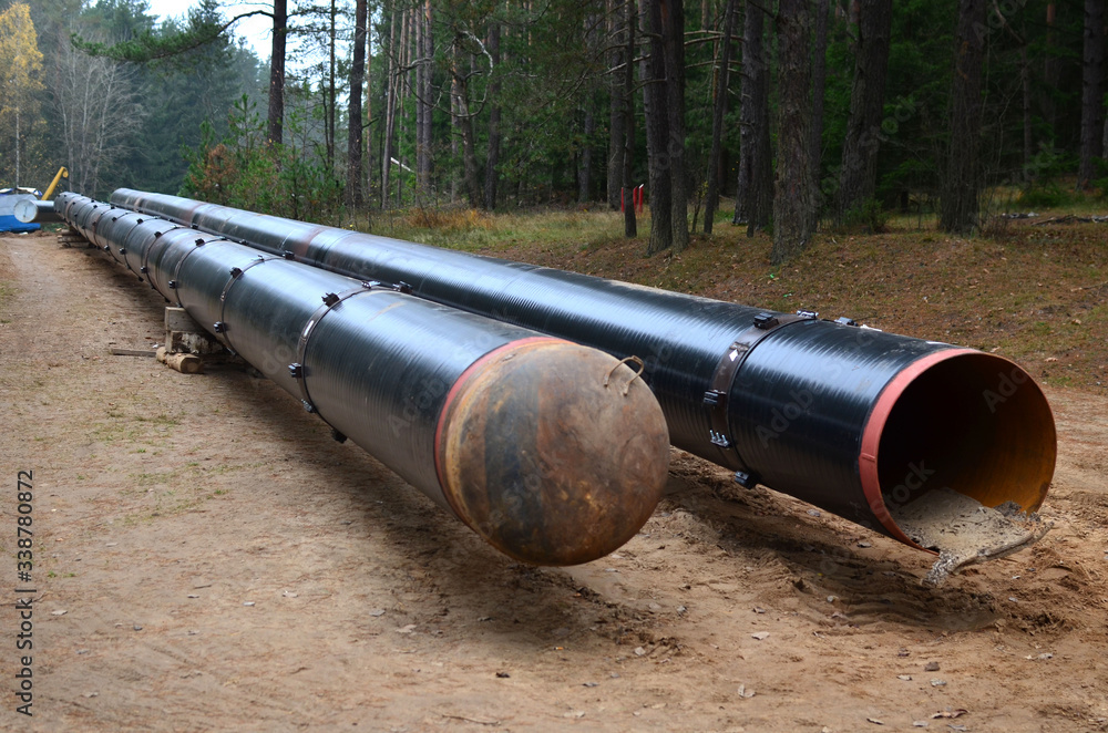 Sections of pipe on top of wooden supports at an construction site for natural gas. Construction of gas pipeline to new LNG plant. Excavated trench to install gas supply pipework for the power station Sections of pipe on top of wooden supports at an construction site for natural gas. Construction of gas pipeline to new LNG plant. Excavated trench to install gas supply pipework for the power station