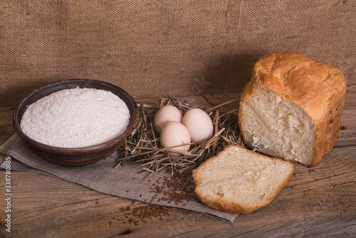 A cut piece of white bread, eggs and flour on a wooden table