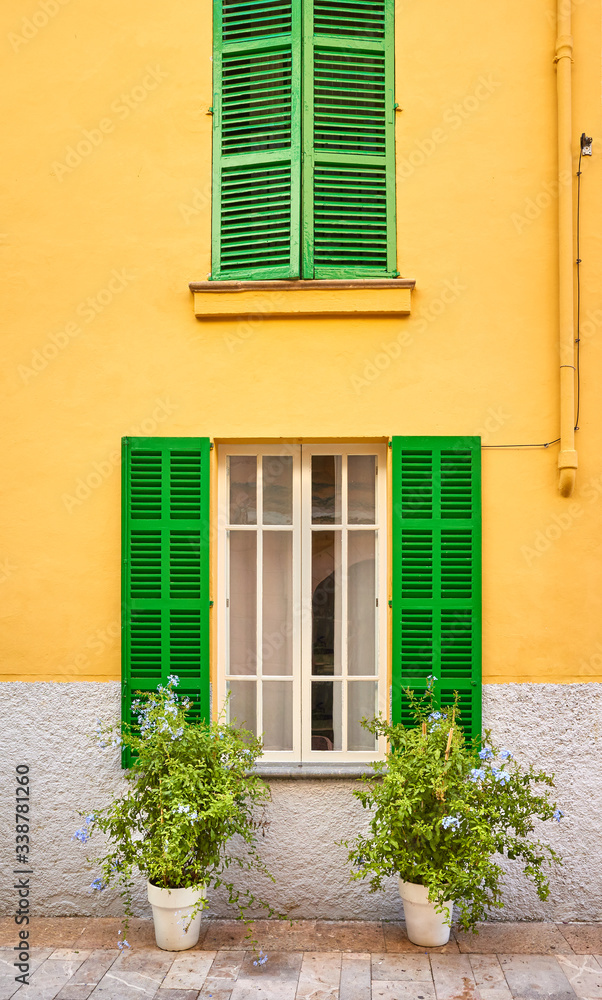 Green wooden shutters on yellow wall by a narrow street in Alcudia, Mallorca, Spain.