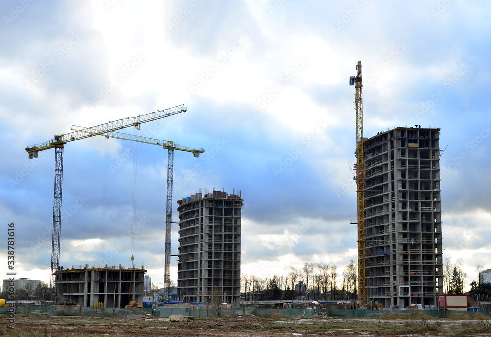 Tower cranes constructing a new residential building at a construction site against blue sky. Renovation program, development, concept of the buildings industry. Tower cranes constructing a new residential building at a construction site against blue sky. Renovation program, development, concept of the buildings industry.