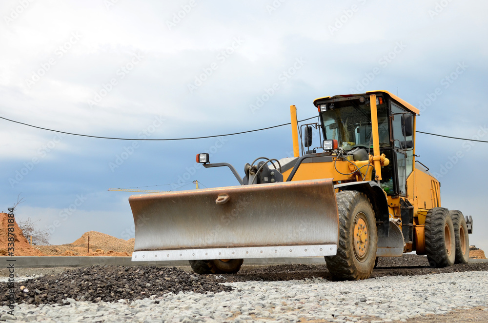 Сonstruction machine Motor Grader at a construction site level the ground and gravel stones for the construction of a new asphalt road. Road construction equipment Сonstruction machine Motor Grader at a construction site level the ground and gravel stones for the construction of a new asphalt road. Road construction equipment