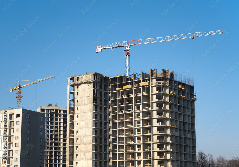 Tower crane constructing a new residential building at a construction site against blue sky. Renovation program, development, concept of the buildings industry.