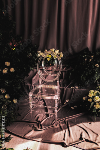 transparent chair in a wedding decor, lit by lateral sunlight, around flowers and rose leaves