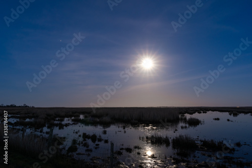 Landscape shot of full moon with rays shining and reflecting in a moor