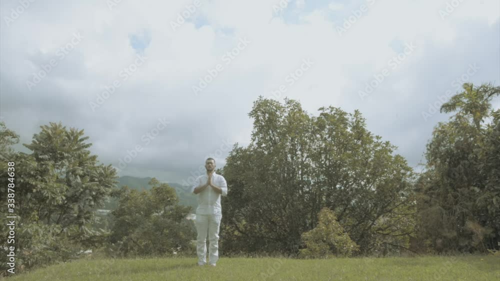 Young man in white Dress doing yoga meditation and spiritual movements in a beautiful green landscape mindfulness and tai chi Young man in white Dress doing yoga meditation and spiritual movements in a beautiful green landscape mindfulness and tai chi