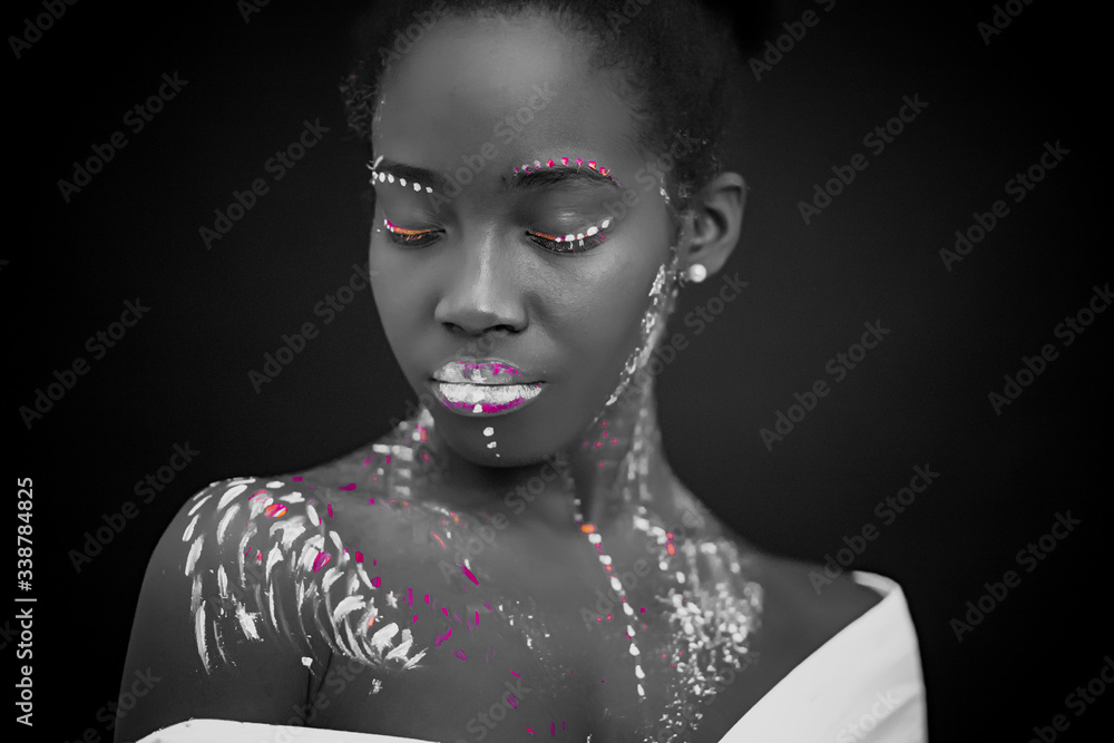 african woman with body art glowing in ultraviolet light. Portrait of beautiful woman painted in fluorescent powder. isolated dark space. black and white photo african woman with body art glowing in ultraviolet light. Portrait of beautiful woman painted in fluorescent powder. isolated dark space. black and white photo