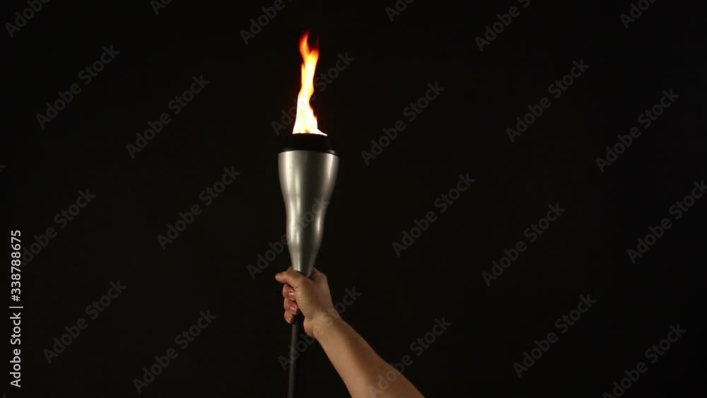 Human hand Lifting and Holding a flaming Torch on a Black Background with flames burning. Stock Video Clip Footage