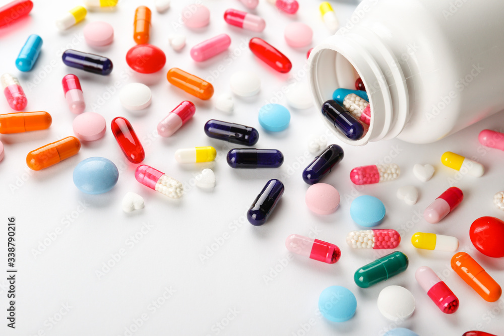 Flat lay composition with bunch of different colorful pills scattered on table from popped plastic bottle. Pile of opened medication on white paper textured background. Close up, copy space for text Flat lay composition with bunch of different colorful pills scattered on table from popped plastic bottle. Pile of opened medication on white paper textured background. Close up, copy space for text