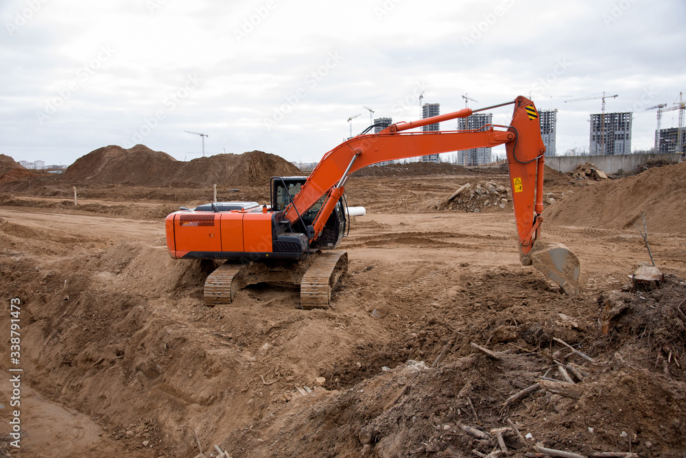 Red excavator during earthworks at construction site. Backhoe digging the ground for the foundation and for laying sewer pipes district heating. Earth-moving heavy equipment