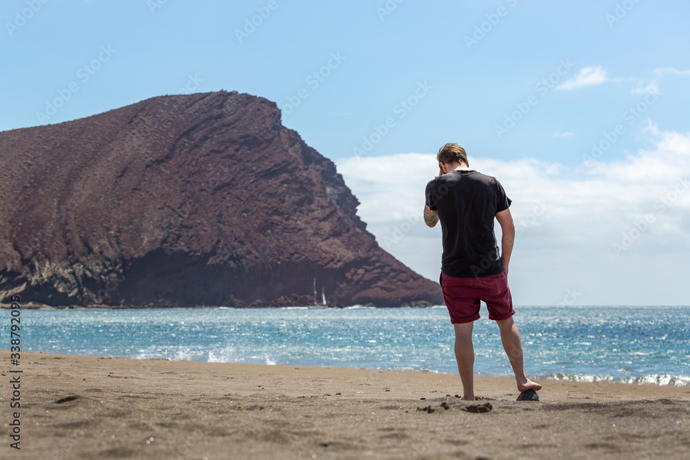 A young handsome man standing on the sand in a beach while touching his head, in Tenerife, Canary Islands, Spain