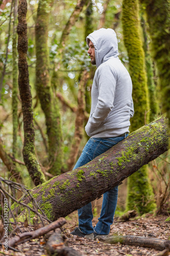 A young man with a hood jacket is walking down through a green and wet forest in Tenerife, Canary Islands, Spain