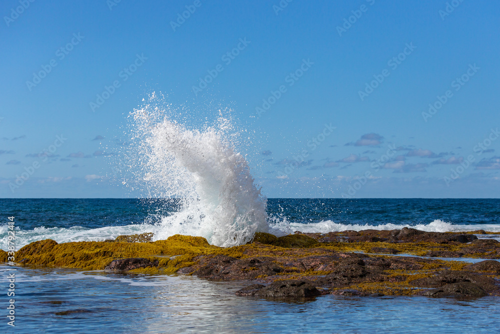 A blue wave breaking into the rocks and making a big splash in Tenerife, Canary Islands, Spain