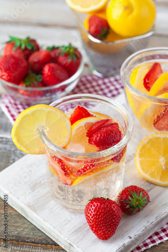 Refreshing homemade lemonade with fresh strawberry, lemon and ice. Healthy cold drink, low calories. Tasty cool summer beverage. Wooden white background, two glasses