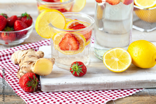 Refreshing homemade sparkling lemonade with fresh strawberry  lemon  ice and ginger. Healthy cold drink  low calories. Tasty cool summer beverage. Wooden white background  red napkin as decor