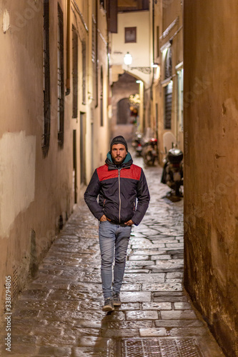 A young handsome bearded man walking by the streets of Florence at night while looking at the camera