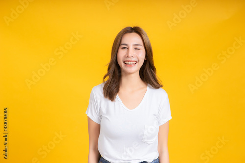 Portrait happy young asian woman laughing blink, wink eye joyful funny positive emotion in white t-shirt, Yellow background isolated studio shot and copy space.