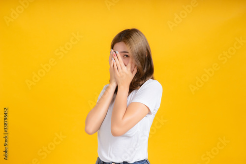Portrait young asian woman covered your hide eye peek looking, scary watching horror movie in white t-shirt, Yellow background isolated studio shot and copy space.