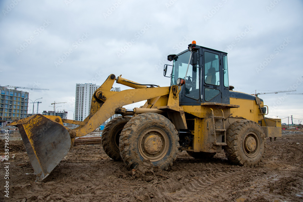 Front-end loader working at construction site. Earth-moving heavy equipment for road work. Public works, civil engineering, road building. Construction machinery for loading, lifting cargo