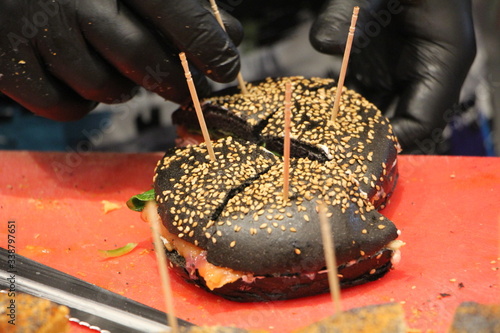 Obraz na plátně Panino al nero di seppia ripieno con salmone e cipolla da mano con guanto nero