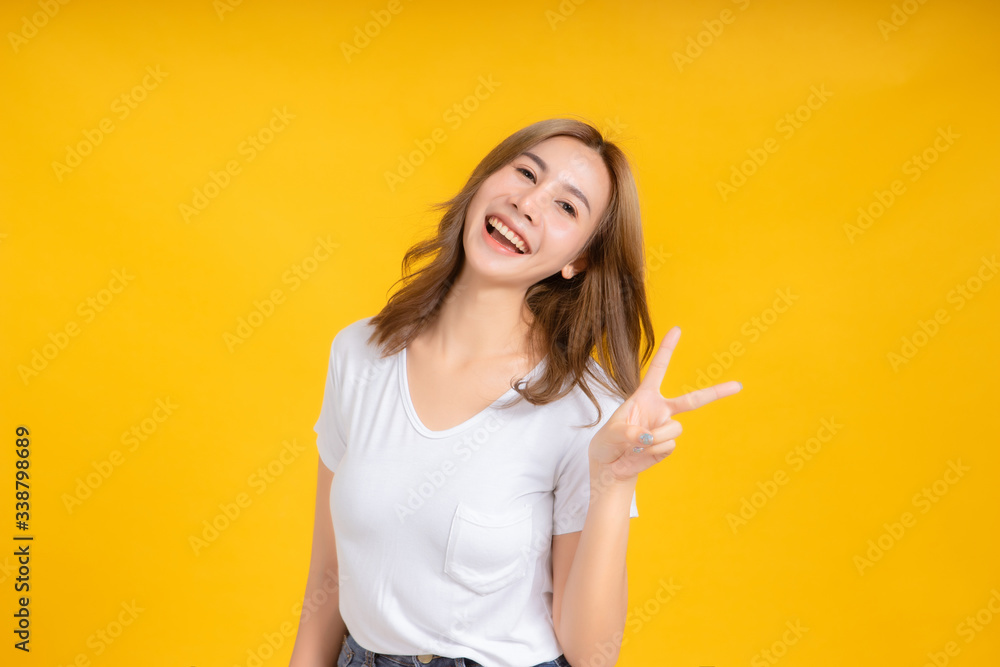 Portrait happy young asian woman laughing finger hands v-symbol gesture selfie joyful funny positive emotion in white t-shirt, Yellow background isolated studio shot and copy space. Portrait happy young asian woman laughing finger hands v-symbol gesture selfie joyful funny positive emotion in white t-shirt, Yellow background isolated studio shot and copy space.