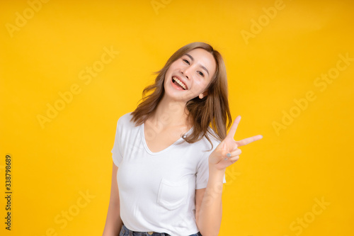 Portrait happy young asian woman laughing finger hands v-symbol gesture selfie joyful funny positive emotion in white t-shirt  Yellow background isolated studio shot and copy space.