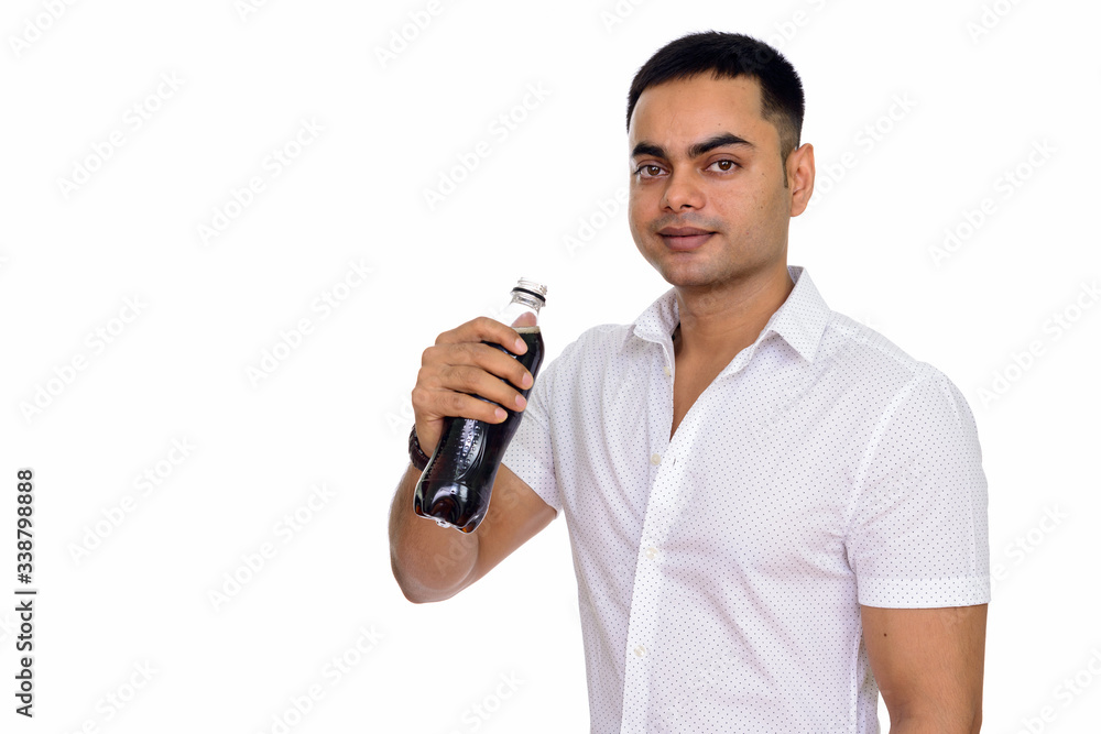 Studio shot of young handsome Indian man drinking soda isolated against white background