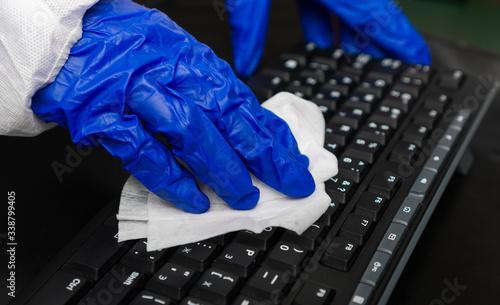 Hand in protective glove with napkin cleaning keyboard. Covid-19 disinfection concept.