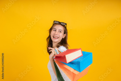 Happy young asian woman with shopping paper bag fashion purchase on store shopping mall concept in white t-shirt smiling emotion on yellow background isolated studio with copy space.