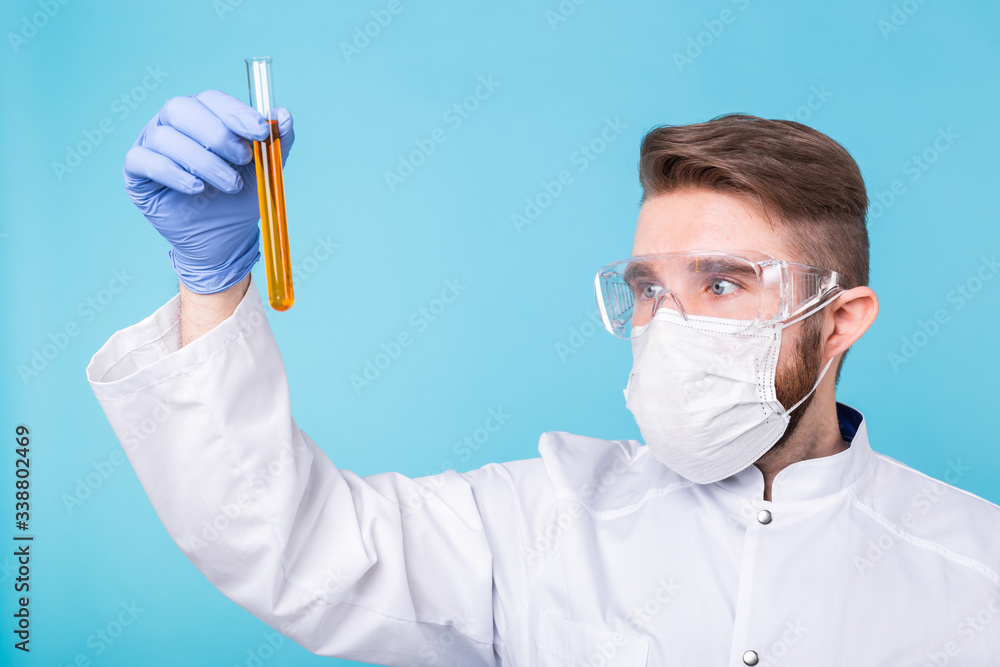 Covid-19, coronavirus, Vaccine development, pandemic, outbreak and medicine concept - Man scientist in flu mask and protective gloves holding a test tube. Covid-19, coronavirus, Vaccine development, pandemic, outbreak and medicine concept - Man scientist in flu mask and protective gloves holding a test tube.