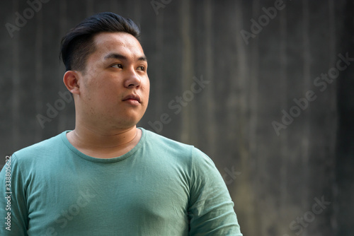 Face of young overweight Asian man thinking outdoors photo