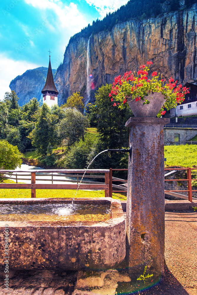 The picturesque landscape with flowers, a waterfall and canyon church in Lauterbrunnen in the Swiss Alps, Switzerland, Europe