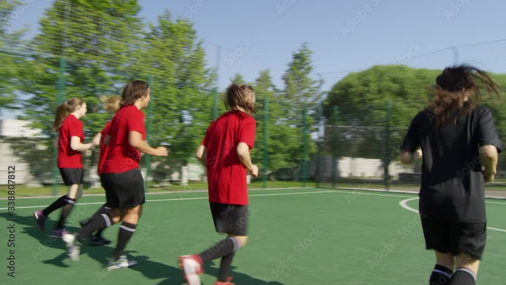 Panning shot of female soccer players in uniform running on field while exercising outdoors on summer day Panning shot of female soccer players in uniform running on field while exercising outdoors on summer day