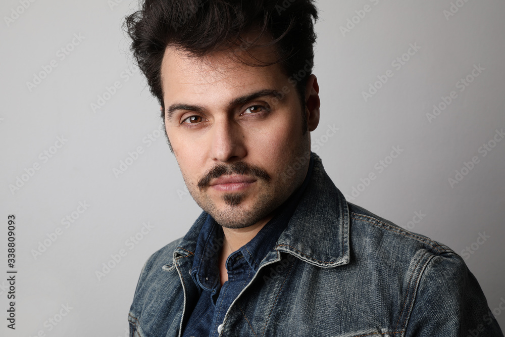 Close-up portrait of serious stylish hipster looks straight with confident expression, wears denim jacket, isolated. Close-up portrait of serious stylish hipster looks straight with confident expression, wears denim jacket, isolated.