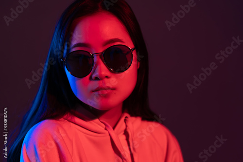 Millennial pretty asian girl with long hairstyle with neon light. Mysterious hipster teenager in glasses.