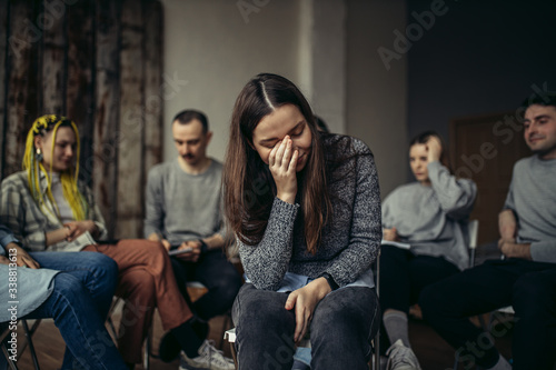 portrait of desperate caucasian woman crying from hopelessness, she needs help from society, suffering from alcohol addict. people sit in circle in the background photo