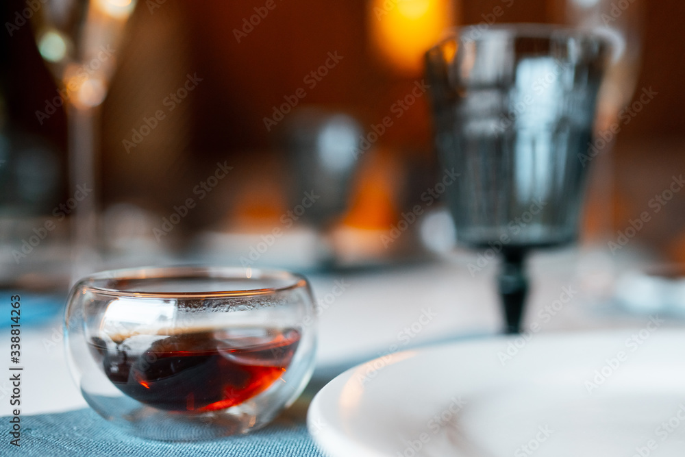 a transparent bowl with black tea on a table in a restaurant. Close-up, blurred background.