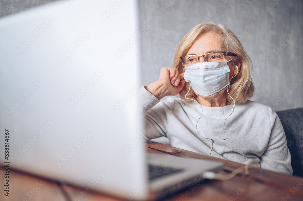 Technology, old age and people concept - lonely sad older senior woman in face medical mask working and making a video call with laptop computer at home during coronavirus COVID19 pandemic. Stay home Technology, old age and people concept - lonely sad older senior woman in face medical mask working and making a video call with laptop computer at home during coronavirus COVID19 pandemic. Stay home