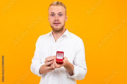 attractive blond European man makes a proposal holding a ring in a box on a yellow background.