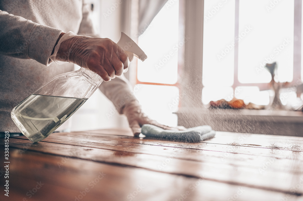 Obraz premium Close up of cleaning home wood table, sanitizing kitchen table surface with disinfectant antibacterial spray bottle, washing surfaces with towel and gloves. COVID-19 prevention sanitizing inside.