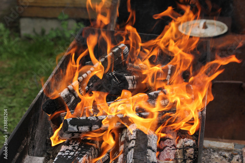 Fire, coals in mangal in the dacha, country. Grill. Green lawn, house. Background image, copy space