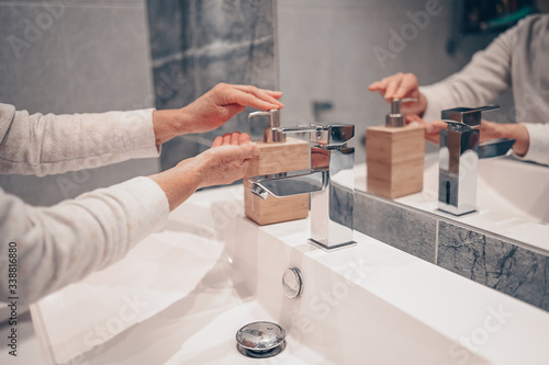 Hand washing lather liquid soap rubbing wrists handwash step senior woman rinsing in water at bathroom faucet sink. Wash hands for COVID-19 spreading prevention. Coronavirus pandemic outbreak.
